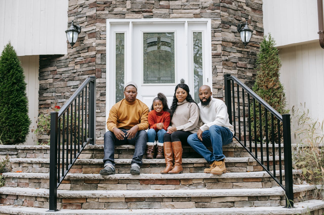 A cheerful family of four sitting on stone stairs outside their house, enjoying a sunny day.